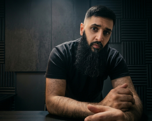 a dark studio perfect background with the owner leaning on a table with a well groomed beard